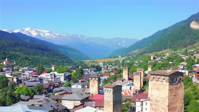 Mestia tower district advances in aerial view beneath snowy Caucasus ridges, supporting Upper Svaneti tourism, medieval defense history, architectural heritage and regional travel marketing.