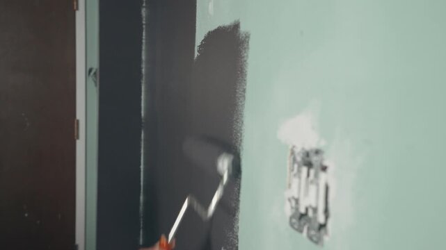 Paint roller applying dark charcoal grey paint over a light green wall during home renovation