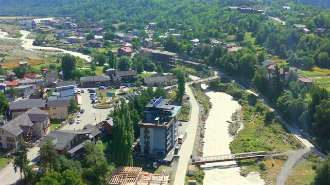 Mountain river winds through forward aerial view across Mestia homes and roads, supporting urban geography, transport planning, river tourism and Georgian regional development media projects.