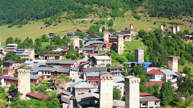 Svan towers advance in aerial view above Mestia homes and hillside fields, supporting medieval heritage, village tourism, architectural preservation and Upper Svaneti destination promotions.