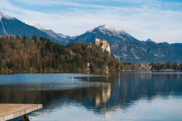 A breathtaking wide panoramic view showcases the perfectly calm Lake Bled, reflecting the majestic castle and surrounding snowy mountains.  © nataliaderiabina