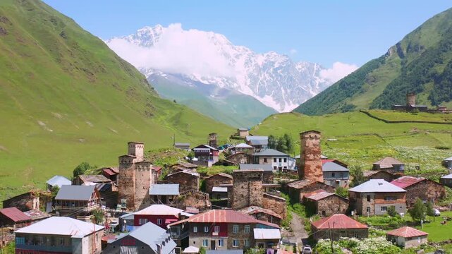 Svan towers approach in forward aerial view above Ushguli rooftops beneath the Shkhara massif, supporting medieval history, heritage tourism, mountain architecture and Georgian destination marketing.