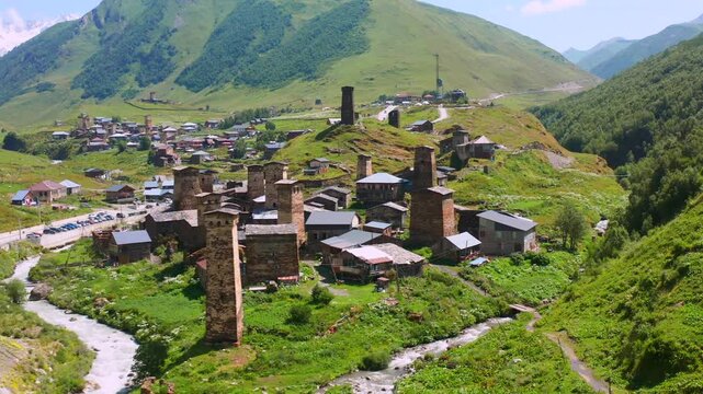 Ushguli village recedes in backward aerial view across the Enguri valley beneath Caucasus ridges, supporting heritage travel, trekking tourism, settlement geography and Georgian destination media.