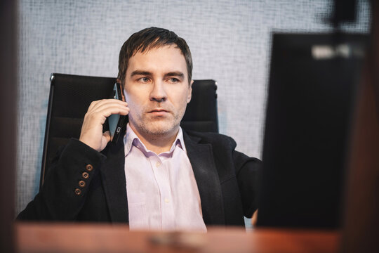 Businessman talking on smartphone while working at computer in office. Professional employee communicating with a client during a business call.