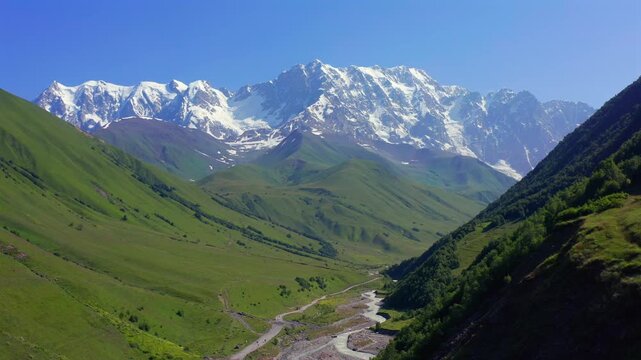 Drone flies backward from Shkhara massif above Enguri valley and green Caucasus slopes near Ushguli, supporting trekking tourism, mountain geography, wilderness travel, Georgian destination promotion