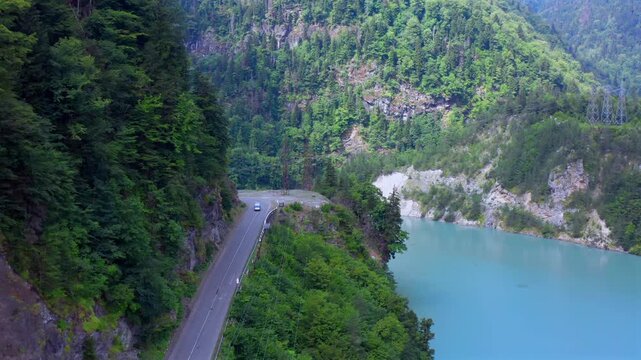 Drone flies forward above Enguri Reservoir road beside turquoise water and forested cliffs in Svaneti, Georgia, supporting scenic driving, transport planning, hydropower geography and mountain tourism
