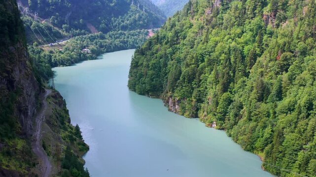 Drone flies forward above Enguri Reservoir through a deep forested gorge in Svaneti, Georgia, supporting reservoir tourism, watershed geography, hydropower context and mountain travel promotion.