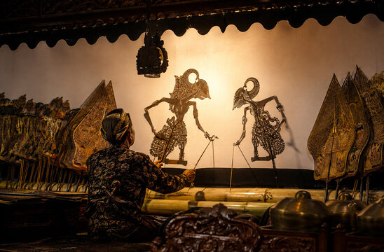 A master puppeteer skillfully manipulates intricate shadow puppets against a backlit screen, illuminating a traditional storytelling performance.