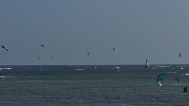 Aerial drone view of kite surfers riding the waves at My Hoa Beach in Vinh Hai, Khanh Hoa, Vietnam, showcasing a spectacular coastal landscape under bright sunlight.
