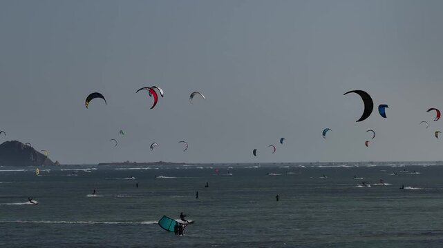 Aerial drone view of kite surfers riding the waves at My Hoa Beach in Vinh Hai, Khanh Hoa, Vietnam, showcasing a spectacular coastal landscape under bright sunlight.
