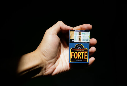 Close up of hand holding Forte Original Full Flavor cigarette pack with Indonesia excise tape isolated on black backround