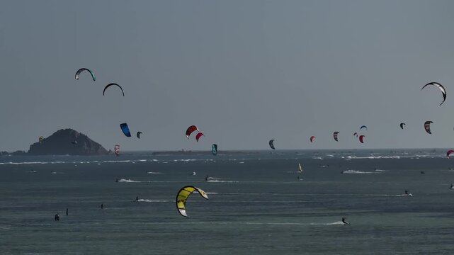Aerial drone view of kite surfers riding the waves at My Hoa Beach in Vinh Hai, Khanh Hoa, Vietnam, showcasing a spectacular coastal landscape under bright sunlight.
