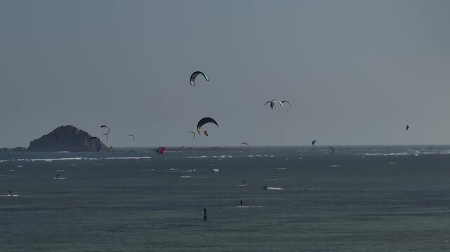 Aerial drone view of kite surfers riding the waves at My Hoa Beach in Vinh Hai, Khanh Hoa, Vietnam, showcasing a spectacular coastal landscape under bright sunlight.
