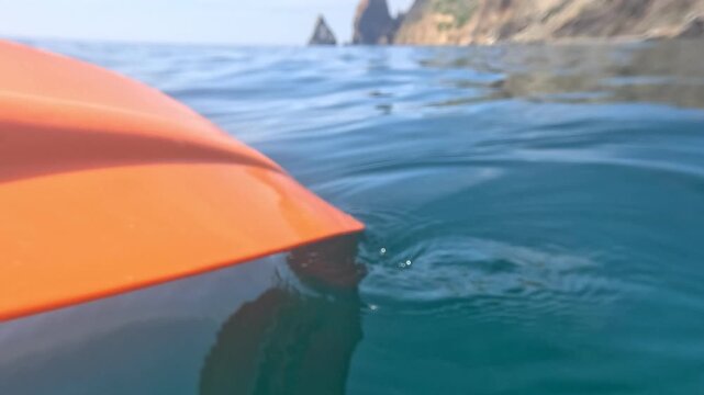 Kayaking ocean adventure featuring an orange kayak gliding through calm turquoise water near scenic coastal cliffs on a sunny day