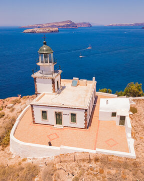 Drone aerial shot of historic Akrotiri Lighthouse on rocky cliff over Aegean Sea in Santorini Greece