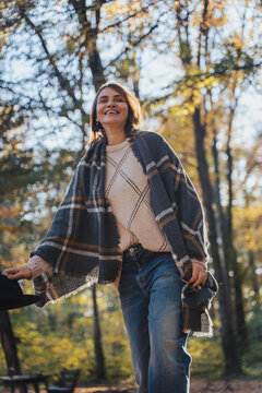 Happy mid-adult woman holding a hat in hands with a joyful smile in autumn forest.