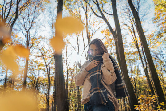 Thoughtful mature female enjoying an autumn walk in the woods while wearing a warm checkered plaid.
