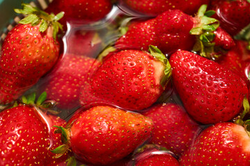 Red strawberries sit in a bowl filled with water. The close-up view shows the texture and shine of the fruit. Light reflects off the surface. This captures the freshness of the strawberries. © bondarillia