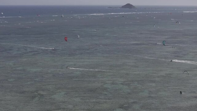 Aerial drone view of kite surfers riding the waves at My Hoa Beach in Vinh Hai, Khanh Hoa, Vietnam, showcasing a spectacular coastal landscape under bright sunlight. 