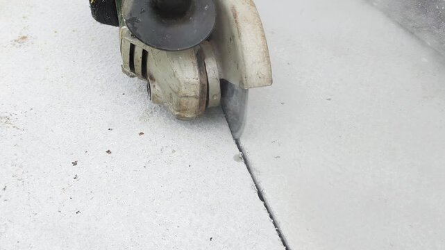 Angle grinder cuts concrete surface creating dusty cloud during construction work. Heavy construction work generates fine dust particles while power tool makes straight line cut on floor indoors.