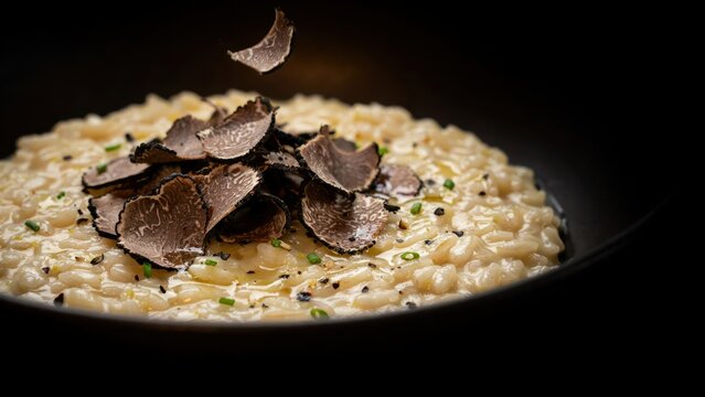Creamy mushroom risotto topped with fresh truffle slices in a dark bowl. This elegant dish represents gourmet dining for luxury restaurant and food marketing campaigns.