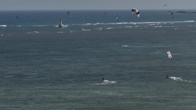Aerial drone view of kite surfers riding the waves at My Hoa Beach in Vinh Hai, Khanh Hoa, Vietnam, showcasing a spectacular coastal landscape under bright sunlight. 