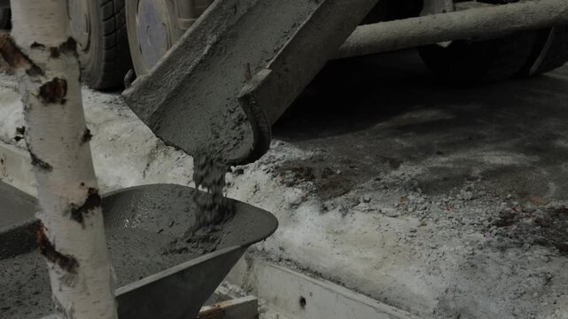 Wet concrete pours from a mixer chute into a wheelbarrow at a construction site, concrete delivery and building process.