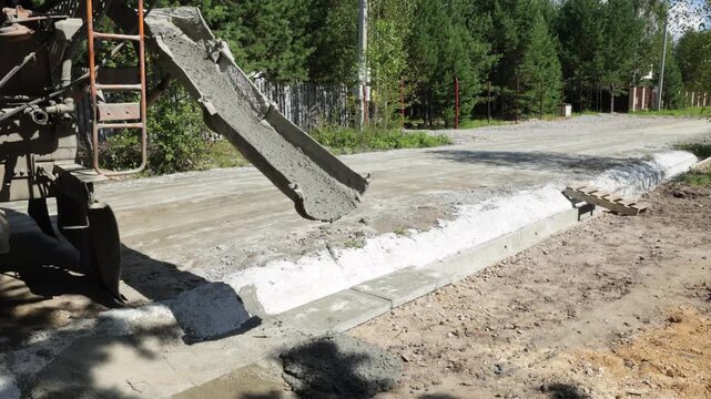 Residual wet concrete drips from a mixer chute onto the ground at a construction site, concrete delivery and construction process.