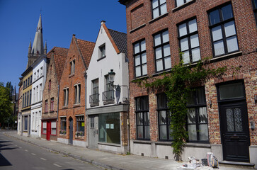 Obraz premium Historic European city street with traditional brick houses, stepped gables and a gothic church tower in the background under a clear blue sky.