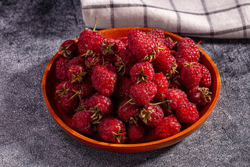 Fresh raspberries in wooden bowl on textured dark surface with checkered cloth background © Andrei Starostin