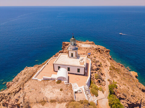 Drone aerial view of historic Akrotiri Lighthouse perched on volcanic rock cliff over Aegean Sea in Santorini Greece