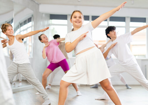 Positive female teenager dances vogue in choreographic school, group of young people in sportswear trains together with their classmates in gym before competitions, battle