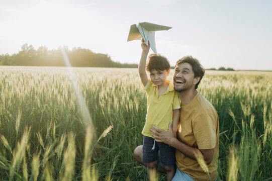 Happy father and boy launch a paper airplane in a summer field