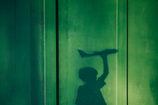 Shadow of a boy holds a toy airplane against a green wall