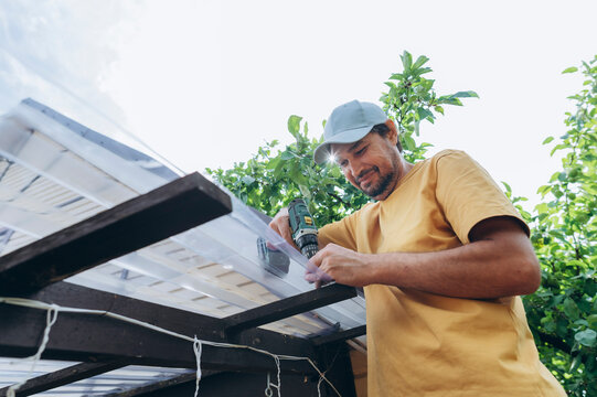 A man repairs a house roof with a power drill outdoors