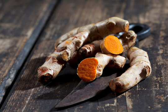Whole and sliced turmeric and an old knife on dark wood