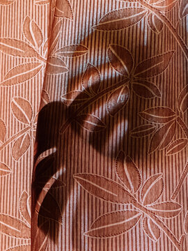 Monstera leaf shadow cast on patterned curtain in warm sunlight, abstract botanical background.