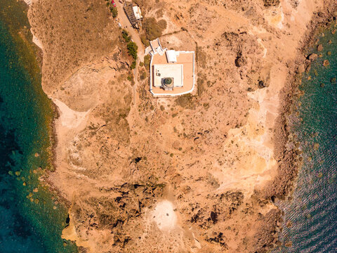 Overhead drone aerial shot of historic Akrotiri Lighthouse on rocky headland in Santorini Greece