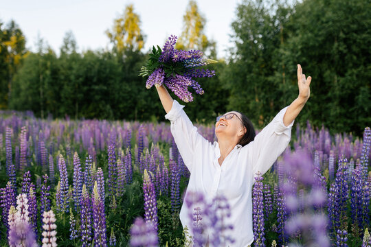 Woman raises lupine bouquet in a blooming summer meadow