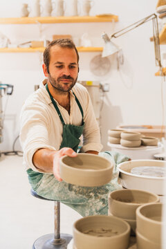 A male potter holds a handmade clay bowl in his workshop