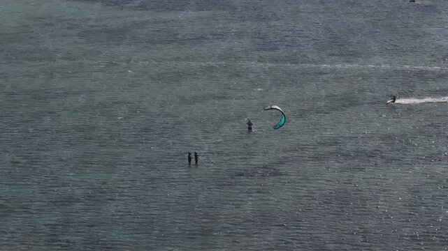 Aerial drone view of kite surfers riding the waves at My Hoa Beach in Vinh Hai, Khanh Hoa, Vietnam, showcasing a spectacular coastal landscape under bright sunlight. 