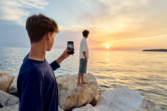 Teenager photographing his brother with a mobile phone at sunset