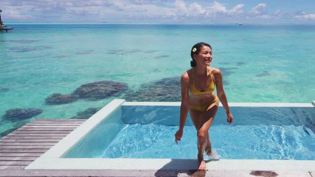 Luxury resort travel vacation destination idyllic overwater bungalow villa woman coming out of pool living luxurious lifestyle. Raw unedited vertical video of real woman model without makeup