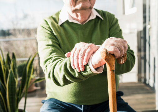 Senior man sitting at the window leaning on cane