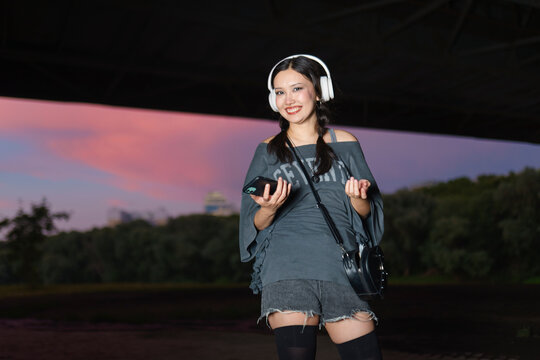 Young woman listens to music with headphone outdoors at sunset