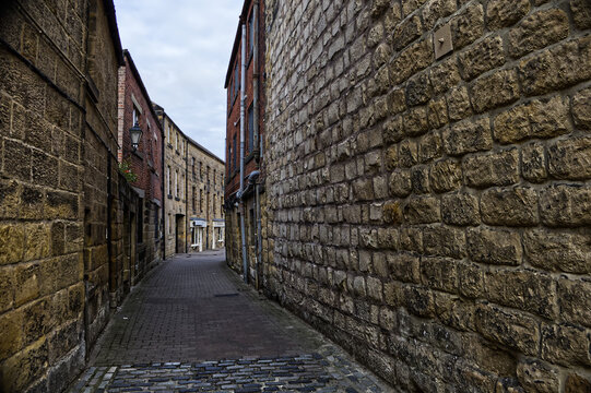 Empty narrow cobbled alleyway between historic sandstone buildings in a traditional European town.