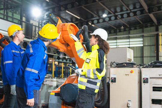 Robotics engineers and technician inspecting industrial robot arm, automation team working together at robotic manufacturing plant, factory operators examining robotic machinery and system in plant