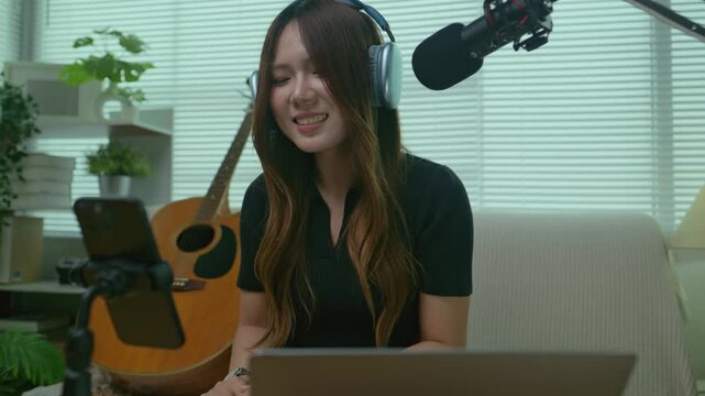Asian female content creator hosts livestream singing video show With a cheerful, bright and happy smile In home studio. Scene for hosting livestream programs remote podcast and music streaming