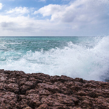 A large wave crashes against a rocky cliff in Sagres Portugal