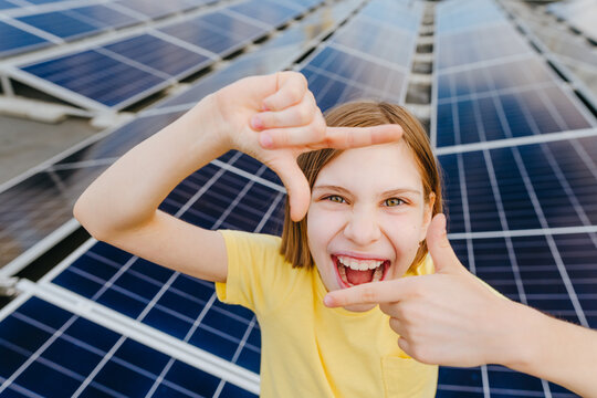 A smiling girl makes a finger frame in front of a solar panel
